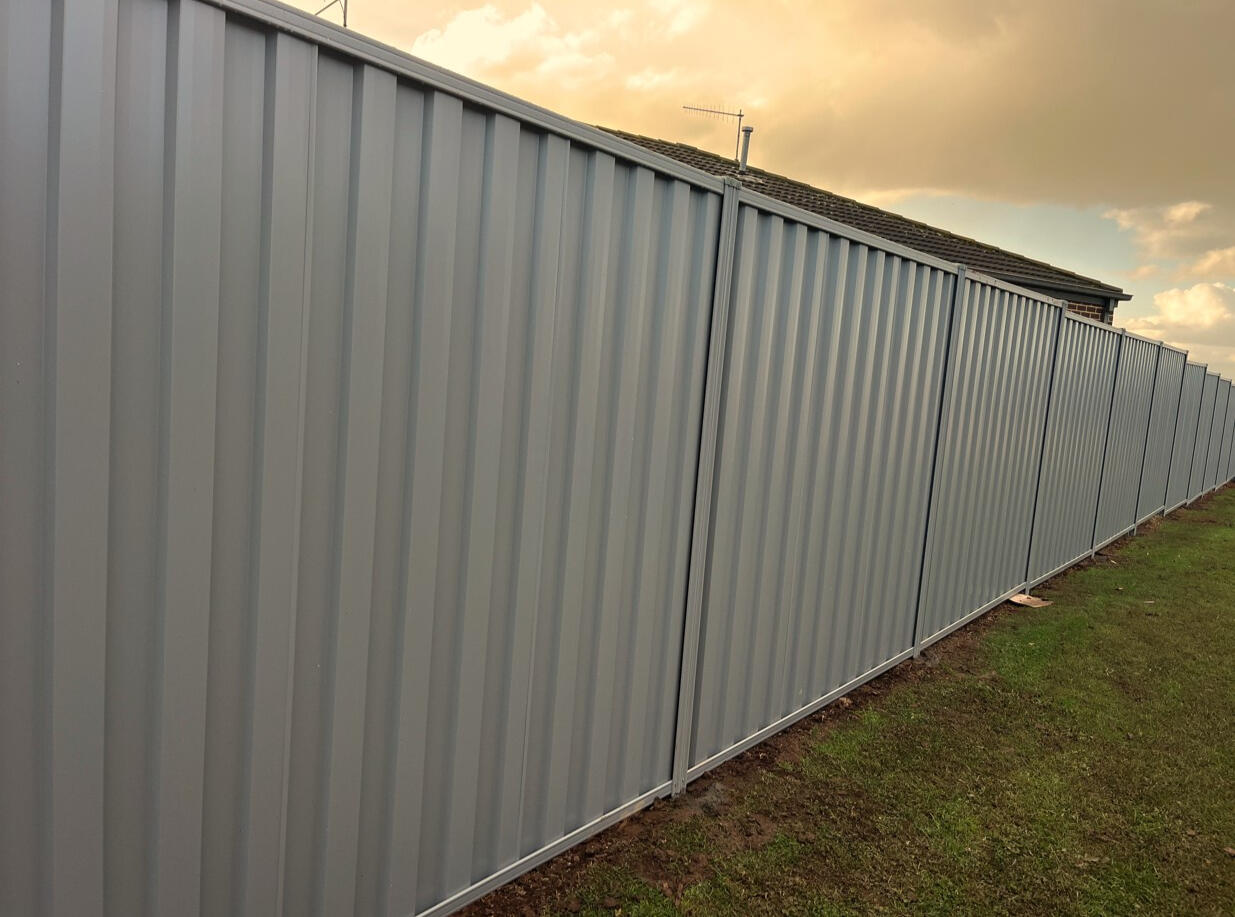 Paperbark Colorbond fence with timber sleepers and stepped panels installed on sloping ground in Berwick 2m high Colorbond privacy fence with timber sleepers and stepped panel design completed for a shared boundary on a sloping block in Berwick.