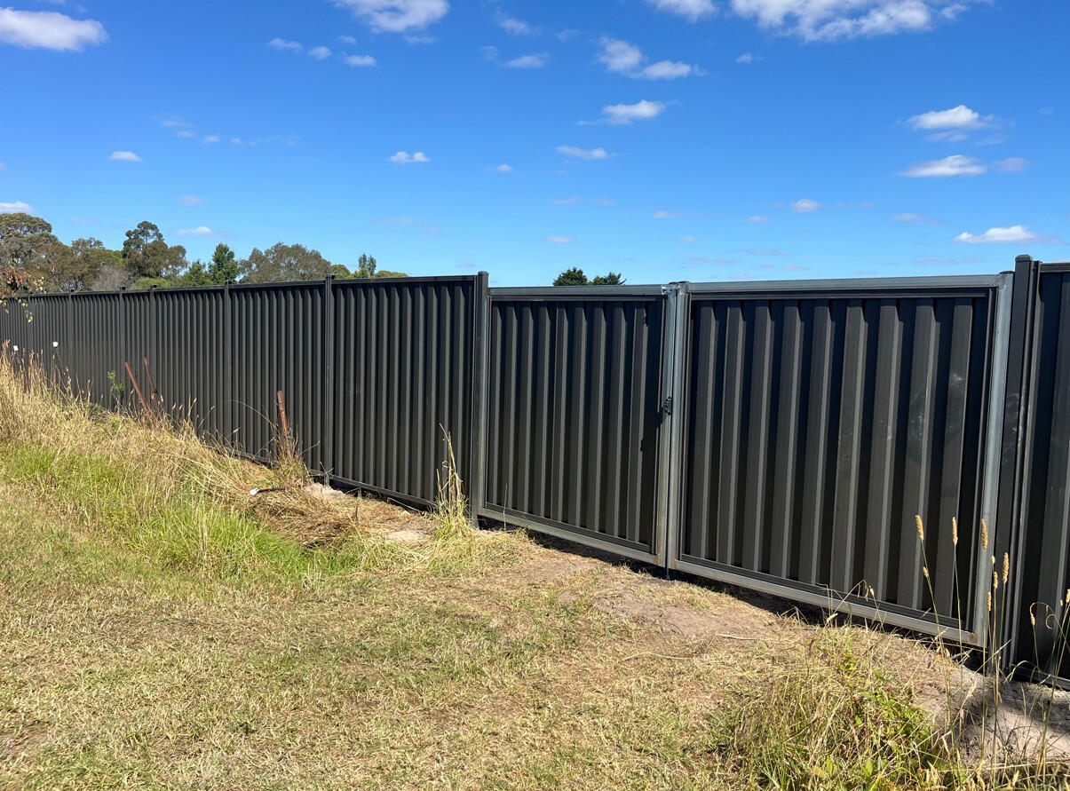 Extra-high 2.1m Monument Colorbond boundary fencing with custom double driveway gates completed in Longwarry for improved rural property security, privacy and vehicle access.