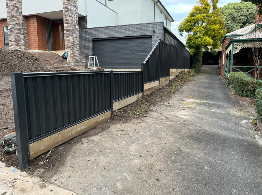 Monument Colorbond fence with stepped panel design and multiple sleepers installed on a steep sloping block in Berwick.