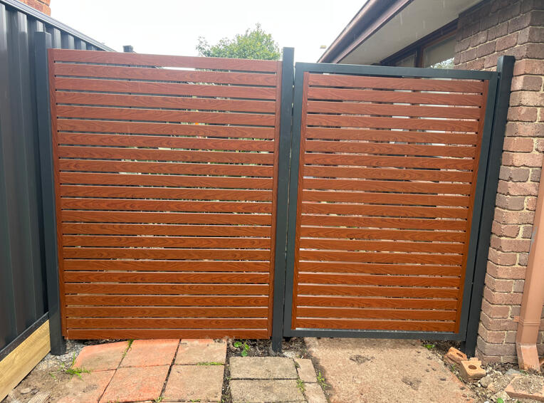 Monument aluminium slat gate with timber-look slats and automatic remote-controlled motor. Custom automated aluminium slat driveway gate completed in Narre Warren South featuring Monument frame, timber-look slats, 10mm spacing and remote-controlled motor system.